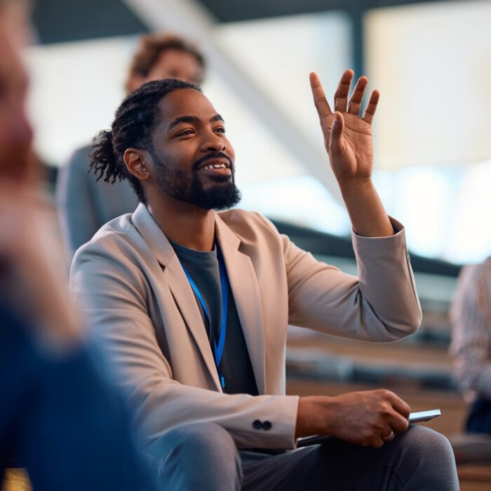 Happy black business seminar attendee asking a question from the audience.